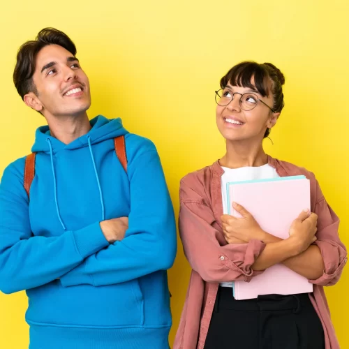 young-student-couple-isolated-on-yellow-background-looking-up-while-smiling